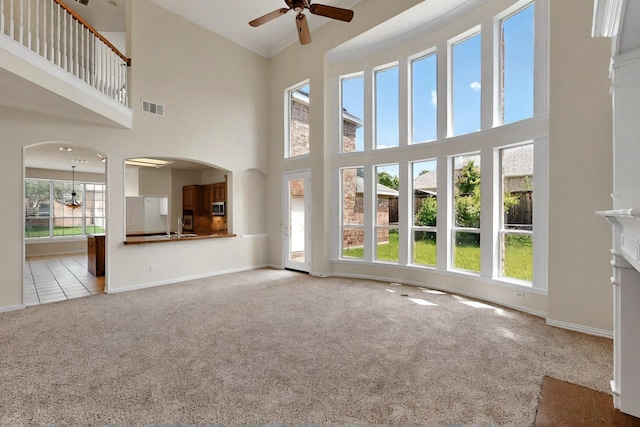 unfurnished living room with ceiling fan, carpet, a high ceiling, arched walkways, and baseboards