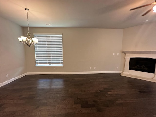 unfurnished living room featuring a chandelier, dark wood-style floors, a ceiling fan, baseboards, and a fireplace with raised hearth