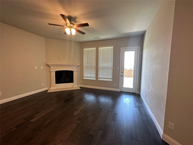 unfurnished living room featuring a ceiling fan, dark wood finished floors, baseboards, and a fireplace with raised hearth