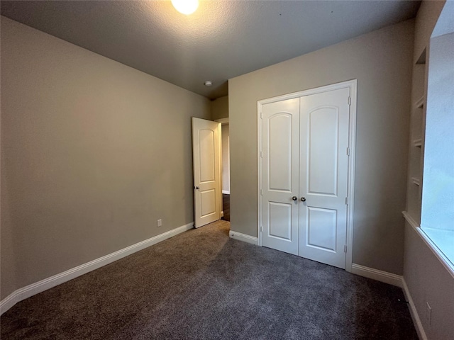 unfurnished bedroom featuring dark colored carpet, a closet, and baseboards
