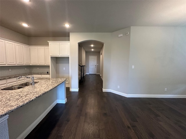 kitchen with a sink, arched walkways, dark wood-style floors, white cabinets, and baseboards