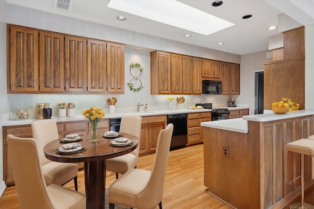 1817 Crockett Cir, Irving, TX 75038 - kitchen with black appliances, a skylight, a peninsula, light countertops, and light wood-style flooring