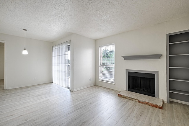 unfurnished living room featuring a textured ceiling, wood finished floors, a fireplace with raised hearth, built in shelves, and baseboards