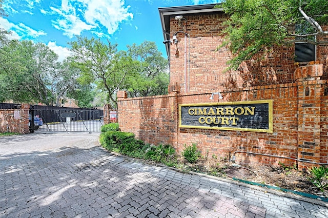 community / neighborhood sign featuring a gate, decorative driveway, and fence