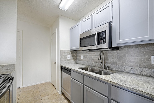 kitchen featuring appliances with stainless steel finishes, a sink, gray cabinets, tasteful backsplash, and a textured ceiling
