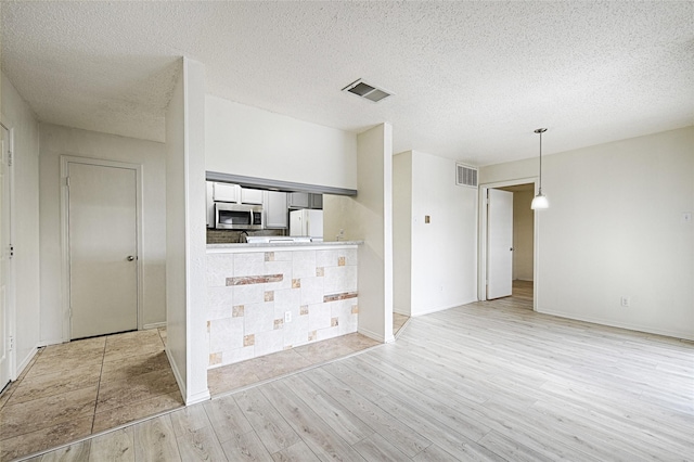 unfurnished living room featuring light wood-style floors, baseboards, and a textured ceiling