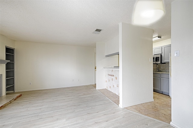 unfurnished living room with a textured ceiling, light wood-type flooring, built in features, and a sink