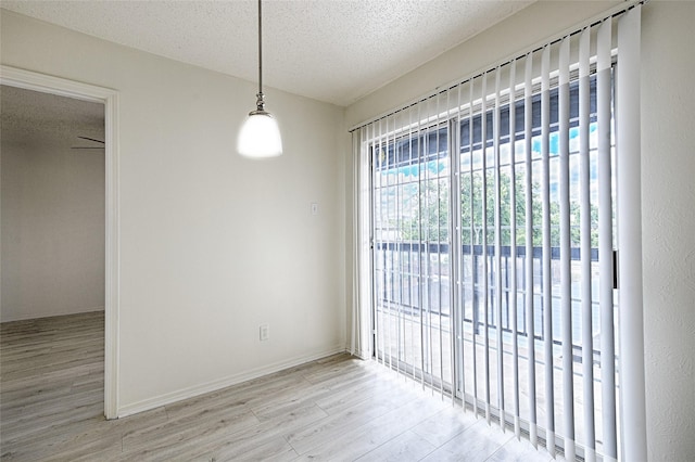 unfurnished dining area featuring wood finished floors, a textured ceiling, and baseboards