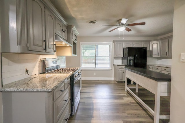 kitchen with stainless steel gas stove, under cabinet range hood, gray cabinetry, black refrigerator with ice dispenser, and a textured ceiling