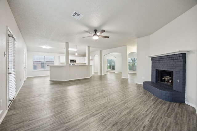 549 Seminole Trl, Murphy, TX 75094 - unfurnished living room featuring ceiling fan, dark wood-type flooring, a brick fireplace, a textured ceiling, and arched walkways