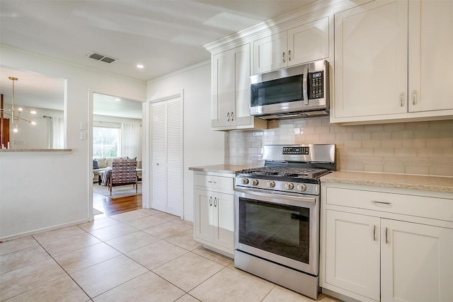 kitchen with stainless steel appliances, backsplash, ornamental molding, light tile patterned floors, and white cabinets