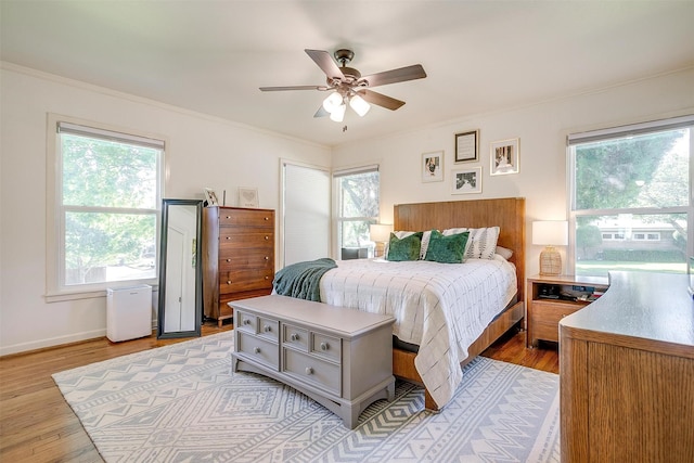 bedroom featuring ornamental molding, light wood-type flooring, a ceiling fan, and baseboards