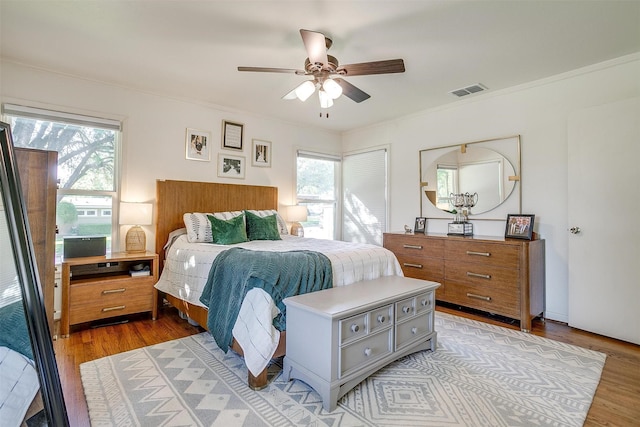 bedroom featuring multiple windows, light wood-type flooring, crown molding, and a ceiling fan