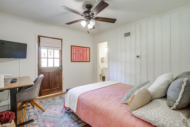 bedroom with wood finished floors, an office area, a ceiling fan, ornamental molding, and connected bathroom