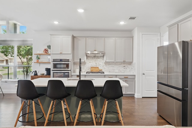 kitchen with stainless steel appliances, under cabinet range hood, dark wood-type flooring, light countertops, and tasteful backsplash