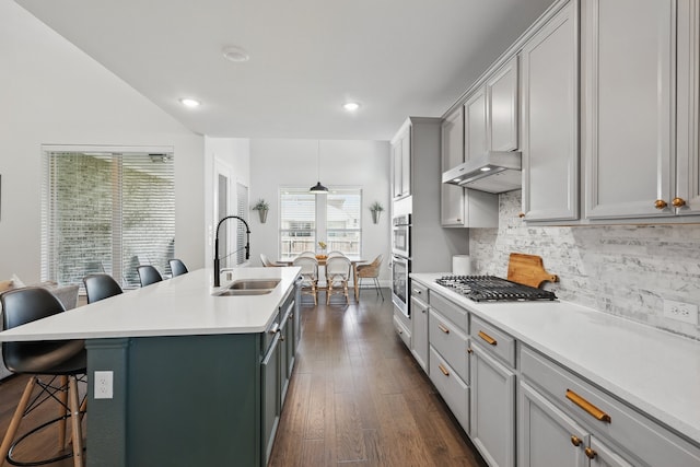 kitchen featuring a sink, stainless steel gas stovetop, a kitchen breakfast bar, decorative backsplash, and a kitchen island with sink