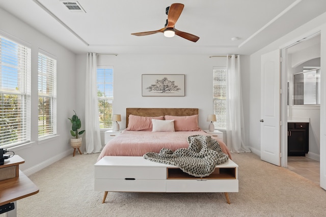 bedroom with multiple windows, light colored carpet, connected bathroom, and baseboards