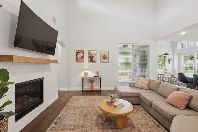 living room featuring a towering ceiling, dark wood-type flooring, a stone fireplace, and baseboards