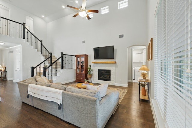living room featuring a high ceiling, a ceiling fan, arched walkways, a glass covered fireplace, and dark wood-type flooring