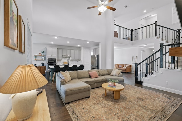living area featuring stairway, a ceiling fan, a towering ceiling, dark wood-style floors, and recessed lighting