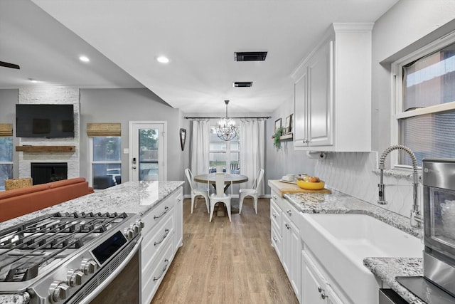 104 Radecke Rd, Krum, TX 76249 - kitchen featuring stainless steel gas stove, a sink, a large fireplace, a chandelier, and light wood finished floors