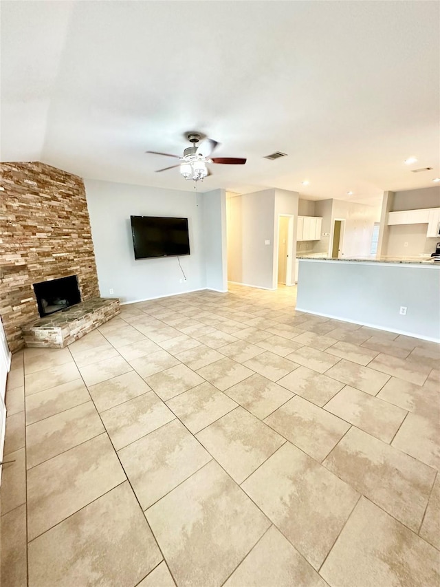 unfurnished living room with light tile patterned floors, a stone fireplace, a ceiling fan, lofted ceiling, and baseboards