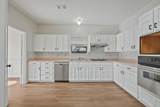 kitchen with appliances with stainless steel finishes, a sink, tasteful backsplash, a textured ceiling, and white cabinetry