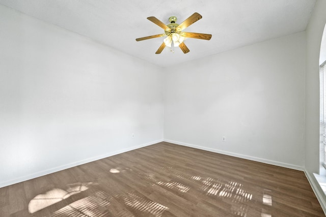 empty room featuring baseboards, a ceiling fan, and dark wood-type flooring