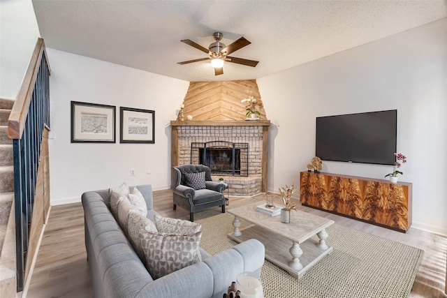 living area with a fireplace, a ceiling fan, wood finished floors, a textured ceiling, and baseboards