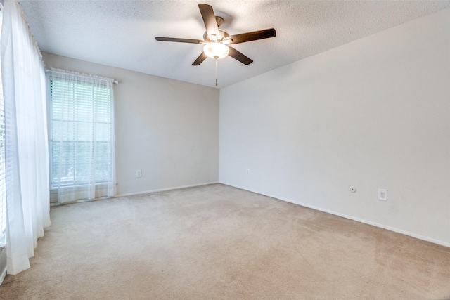 spare room featuring a ceiling fan, light colored carpet, a textured ceiling, and baseboards