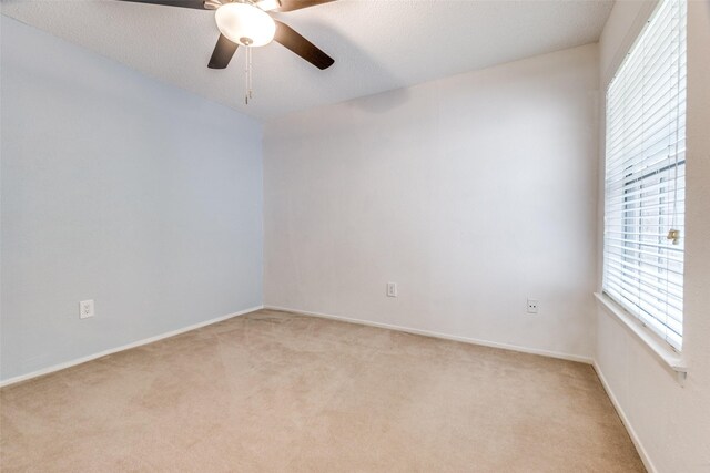 spare room with a ceiling fan, light colored carpet, and baseboards