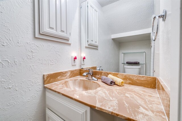 half bath featuring a textured wall, vanity, and toilet