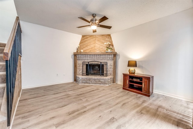 unfurnished living room with ceiling fan, a brick fireplace, wood finished floors, stairs, and baseboards