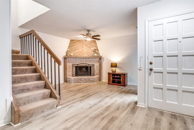 entrance foyer with ceiling fan, wood finished floors, a brick fireplace, stairway, and a textured ceiling
