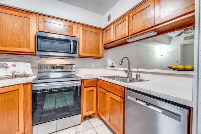 kitchen featuring appliances with stainless steel finishes, a sink, light tile patterned flooring, decorative backsplash, and light countertops