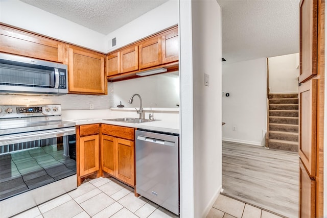 kitchen featuring appliances with stainless steel finishes, a sink, a textured ceiling, light countertops, and light tile patterned floors