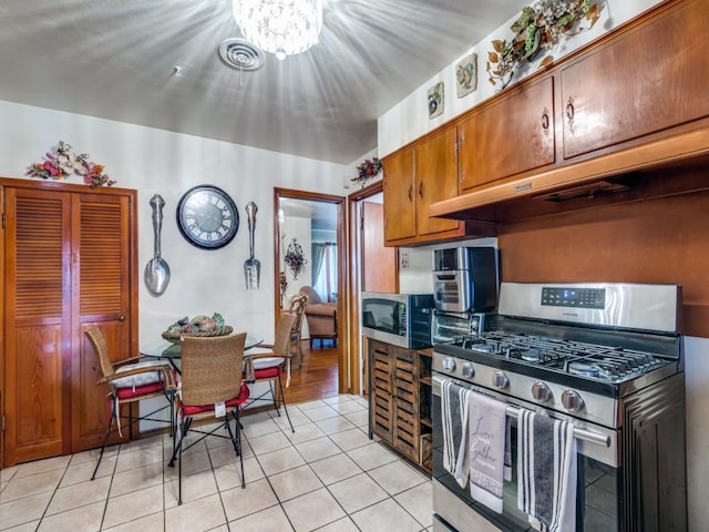 6802 Seco Blvd, Dallas, TX 75217 - kitchen featuring appliances with stainless steel finishes, light tile patterned floors, brown cabinets, under cabinet range hood, and a chandelier