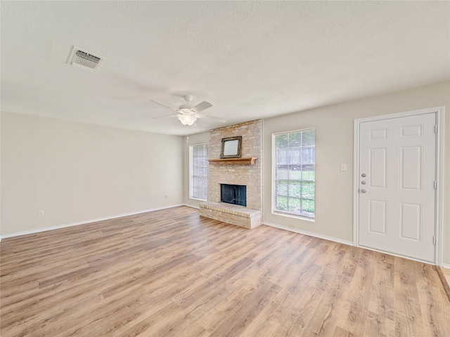 unfurnished living room featuring light wood-style flooring, a ceiling fan, a textured ceiling, baseboards, and a fireplace