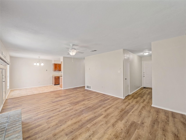 unfurnished living room with light wood-type flooring, a ceiling fan, a chandelier, and baseboards