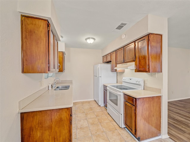 kitchen with white appliances, a sink, under cabinet range hood, brown cabinetry, and light countertops