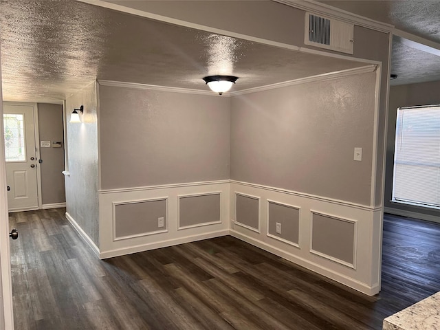unfurnished room featuring dark wood finished floors, a textured ceiling, crown molding, and a wainscoted wall