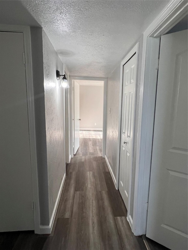 corridor featuring a textured ceiling, dark wood finished floors, and baseboards