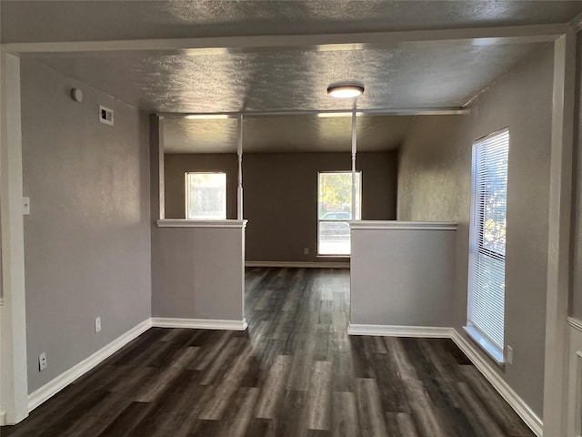 unfurnished dining area with dark wood-style flooring, baseboards, and a textured ceiling