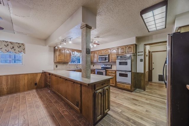 2011 Woodlawn St, Gainesville, TX 76240 - kitchen featuring stainless steel appliances, wainscoting, a peninsula, light wood-style flooring, and ceiling fan