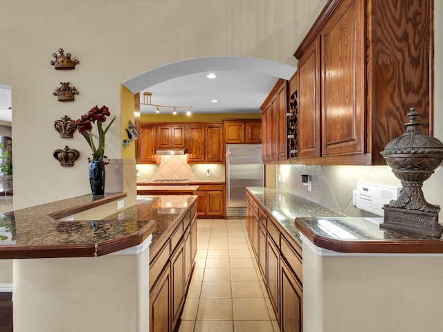 1217 Mandeville Dr, Murphy, TX 75094 - kitchen featuring stainless steel built in fridge, arched walkways, brown cabinetry, a peninsula, and backsplash