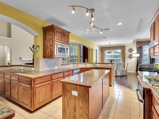 1217 Mandeville Dr, Murphy, TX 75094 - kitchen featuring arched walkways, a peninsula, appliances with stainless steel finishes, a kitchen island, and a sink