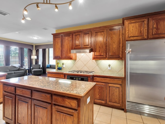 1217 Mandeville Dr, Murphy, TX 75094 - kitchen featuring stainless steel appliances, under cabinet range hood, a kitchen island, light tile patterned floors, and decorative backsplash
