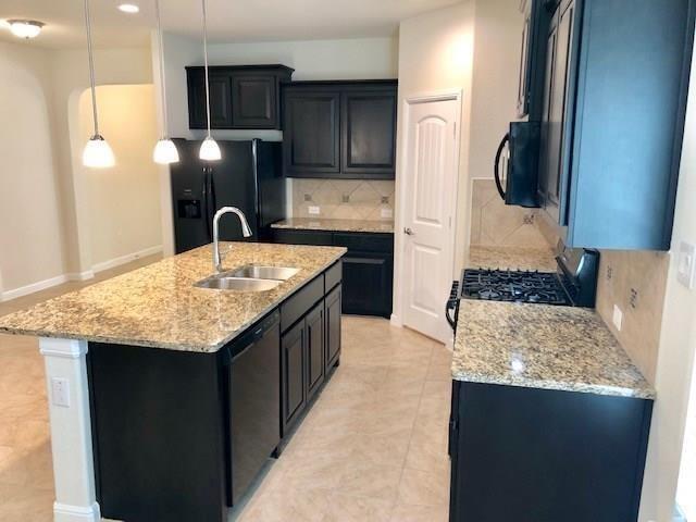 9105 Edenberry Ln, Fort Worth, TX 76179 - kitchen with a sink, black appliances, tasteful backsplash, light stone counters, and a center island with sink