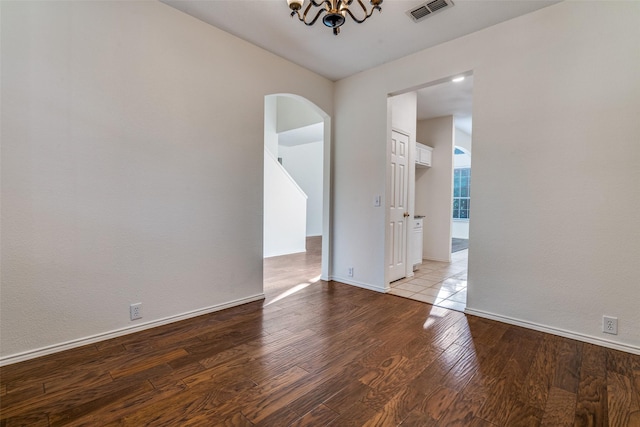 spare room featuring arched walkways, wood finished floors, a chandelier, and baseboards