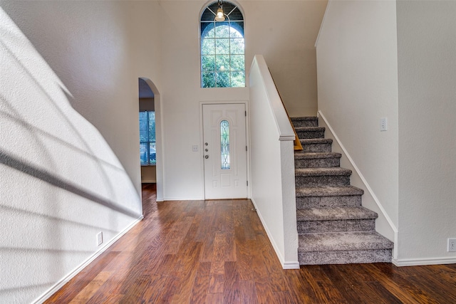 foyer entrance with arched walkways, wood finished floors, stairs, baseboards, and a towering ceiling